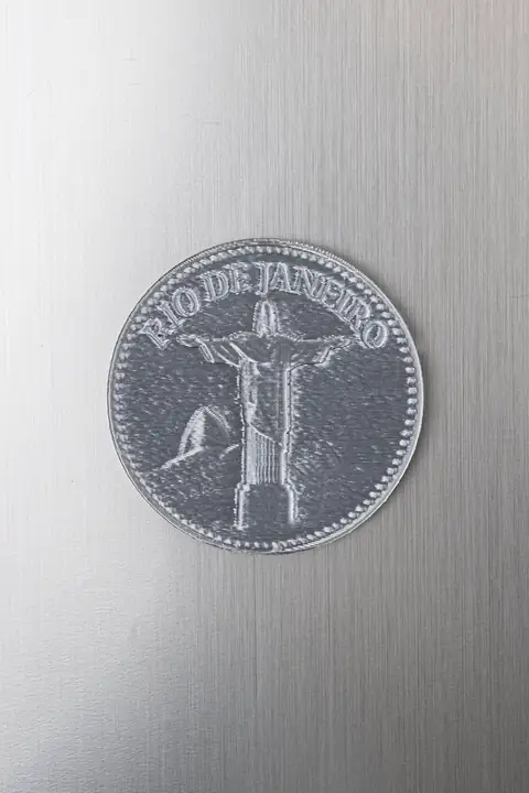 Moeda-souvenir do Rio de Janeiro com acabamento prateado, sobre uma base metálica.